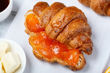 Fresh sweet croissants with butter and apricot jam for breakfast. Continental breakfast on a white concrete table