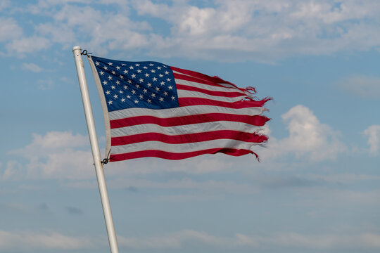 Tattered American flag against blue sky with white clouds in rural Minnesota USA
