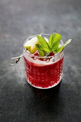 Red cocktail, drink with ice cubes, garnished with mint and lemon, on black stone background, selective focus.