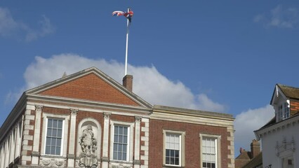Slow motion 4K 60fps shot of a Union Jack flag flying over the Guild Hall in Windsor, Royal Berkshire. 
A dark cloud is seen creeping towards the top of the frame.