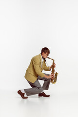 Portrait of young man in stylish yellow jacket playing saxophone isolated over white background....