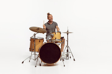 Portrait of funny emotive man playing drums, performing isolated over white background. Bass, rock music