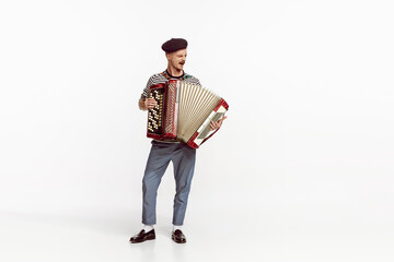 Portrait of young man playing accordion, posing isolated over white studio background. Countryside music