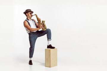 Portrait of stylish man in hat and suglasses playing saxophone , performing isolated over white...