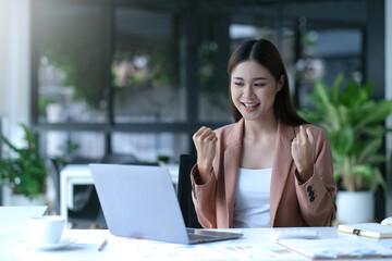 young Asian businesswomen show joyful expression of success at work smiling happily with a laptop computer in a modern office.