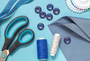 Sewing tools for tailoring on a blue background. Fabric, scissors, buttons, centimeter, pins,...