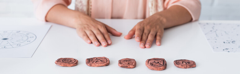 partial view of fortune teller sitting near clay runes and star charts, banner.