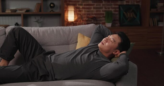 Calm Asian man relaxing on sofa at home after working day