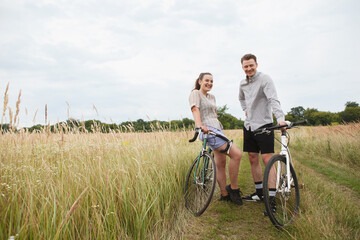 Obraz premium The happy couple cycling near the field. Cyclists man and a woman with bicycles go near the fields in summer.