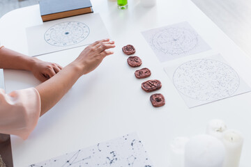 high angle view of cropped astrologist near star charts and clay runes on table.