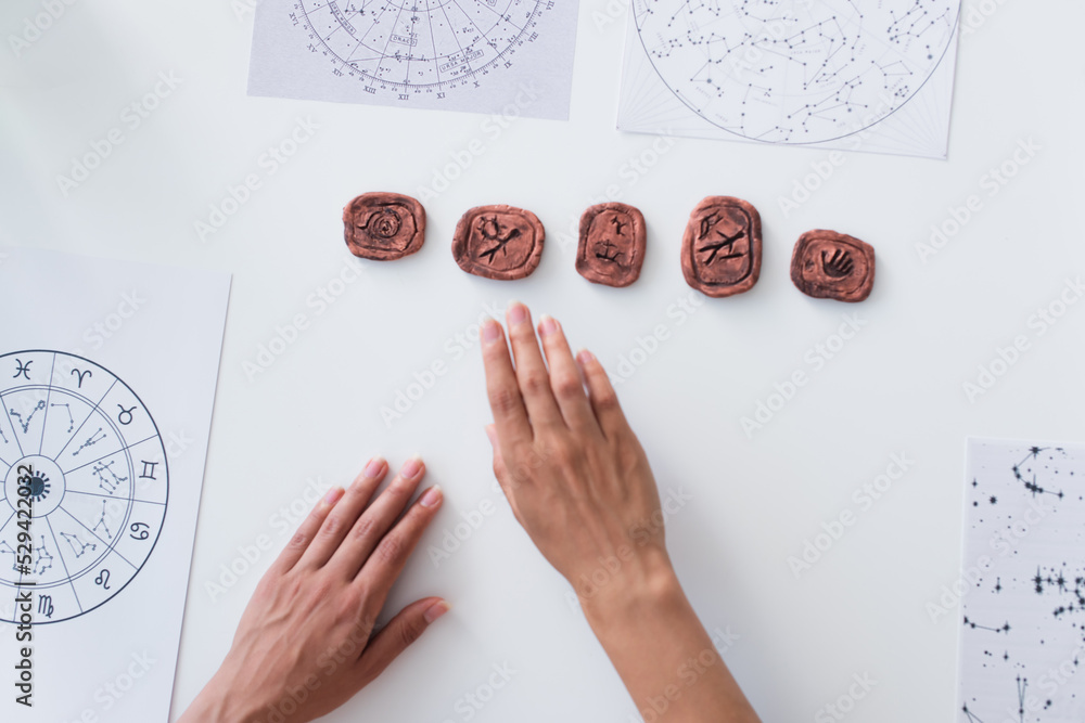 Wall mural top view of cropped oracle near clay runes and star charts on table.