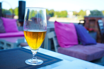 Selective focus of a glass with cold beer in a street cafe with flowers on the embankment in the city. A calm appearance on a sunny summer day.