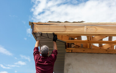 Workers install metal roofing on the wooden roof of a house.