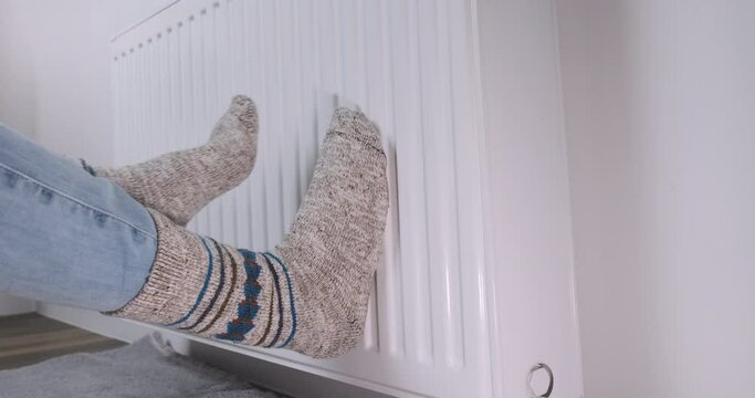 Family in warm socks warms feets on radiator. People put legs on warm battery, side view. Cold in apartment, low heating temperature in house. Europe gas problems. Low temperature in chilly room video