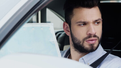 Fototapeta premium young bearded man looking away while sitting in car with map.