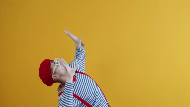 Male mime performer looks up and in a panic puts his hands out in front of him, slowly sinking down as if crushed by an invisible weight. Stress, pressure concept, studio shot on yellow background