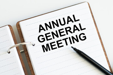 On a light background, a white notebook with are words AGM Annual General Meeting and a pen.