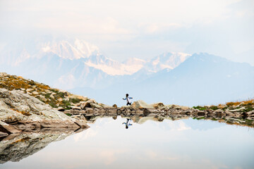 Woman figure solo jump from stone to rock on cliff viewpoint walk explore mountains in fall caucasus range background in Racha, Georgian region. Udziro lake hiking trail