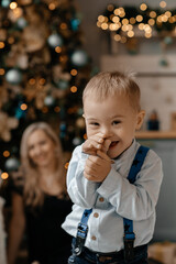 Portrait of a little boy in a white shirt with suspenders, Down Syndrome. Mom with son in new year...