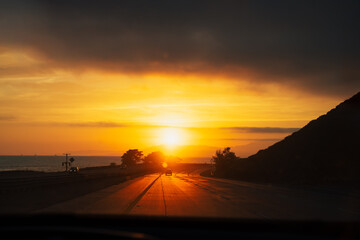 Stunning golden orange sunset on highway 101 California with few cars ocean and mountains. Road...