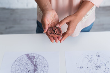 Obraz premium partial view of astrologer holding clay rune near blurred celestial charts.