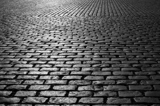 Old cobblestones on Market place “Grote Markt“ in Antwerp Belgium. Shiny historic basalt ashlars and blocks reflecting sunshine. Pavement background, black and white greyscale with high contrast.
