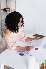 brunette astrologer looking at star charts near clay runes and prediction book.