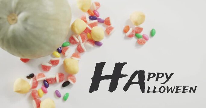 Animation of halloween text over pumpkin bucket with sweets on grey background