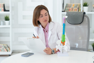 Young attractive female doctor orthopedist demonstrating the problem on spine bone model on the...