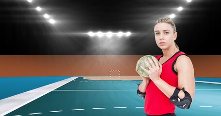 Portrait of confident young female caucasian handball player holding ball at illuminated stadium