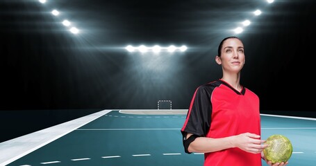 Confident smiling caucasian female player holding ball while looking away at illuminated stadium