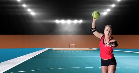 Portrait of muscular female caucasian handball player throwing ball at illuminated stadium
