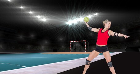 Focused caucasian female handball player pointing while throwing ball at illuminated stadium