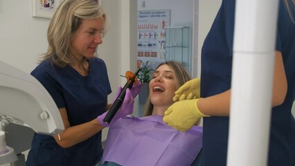 Female dentist with assistant working in dental clinic examining patient teeth.