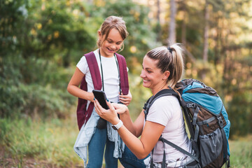 Mother and daughter using map on mobile phone and enjoy hiking together.