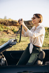 Woman road tripping by cabriolet and making photos on camera