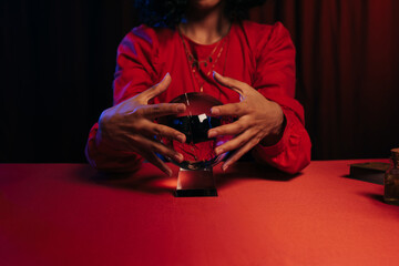 cropped view of medium holding hands near crystal ball during spiritual session on dark background.