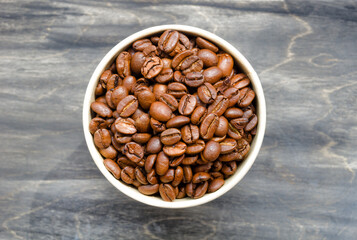 Roasted coffee beans in a paper cup on a black table.