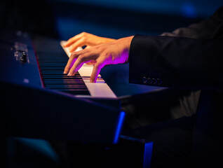 Hands of a man are playing on an electric piano keyboard in dark environment