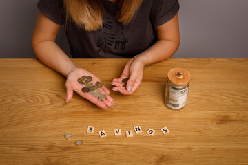 Woman holding and counting zloty coins in front of her is inscription savings.
financial concept of saving and indebtedness.