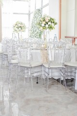 Vertical of white decorated tables with transparent chairs and flowers at a wedding ceremony