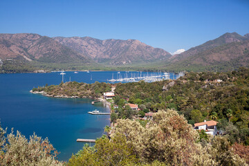 Fototapeta na wymiar Landscape view of sea bay with marina in Turkey from above. Seascape with blue sea water and mountains with green trees.