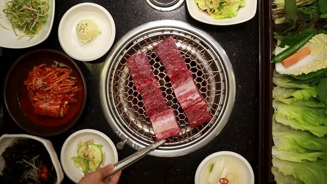 A scene where a female employee's hand puts the fresh Ribs meat galbi on a charcoal-grilled pan Used in a Korean Japanese Asian BBQ restaurant