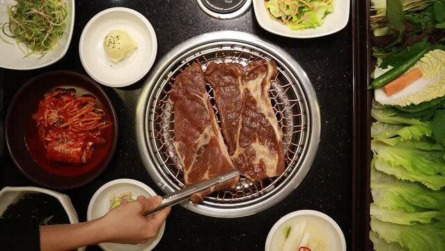A scene where a female employee's hand puts the Seasoned Pork Ribs meat yangnyeomgalbi on a charcoal-grilled pan Used in a Korean Japanese Asian BBQ restaurant
