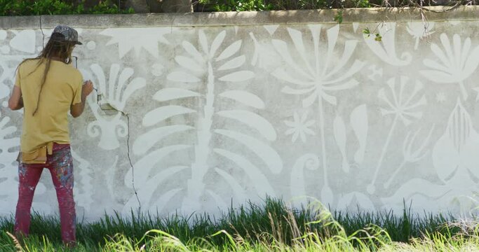 Video of rear view of caucasian male artist with dreadlocks painting mural on wall