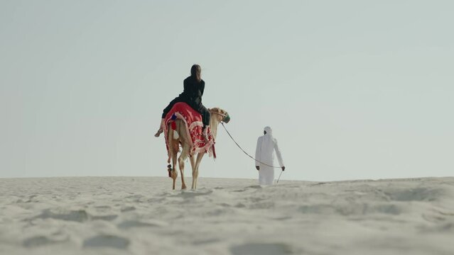 tourist woman riding camel with cameleer leading
