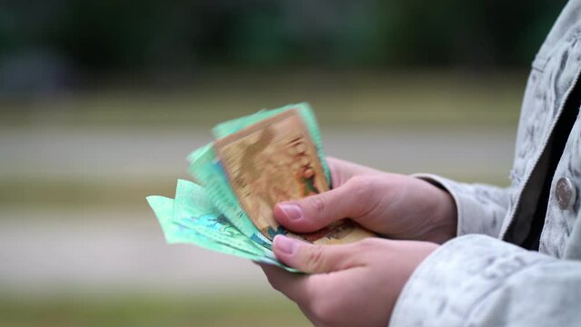 Kazakh woman stands near the roadway and counts the balance of tenge money