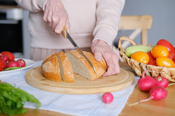 Age healthy woman cuts into pieces whole unleavened bread for breakfast or snack. View from above