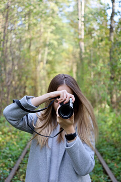 Girl photographer at work. Portrait of a girl photographer with a camera who is busy taking a photo. A beautiful girl in a gray coat takes pictures on the camera.