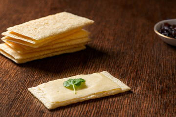Crunchy crisp bread with a layer of cheese on top and a stack in the background on a wooden worktop